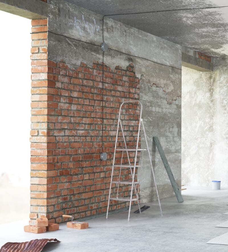 Wohnraum vor der Sanierung: freigelegtes Mauerwerk, beschädigte Decke und offener Estrich